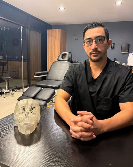 Dr. Kevin Matheus Flores Moraz, cirujano maxilofacial, en su consultorio junto a un modelo 3D de cráneo